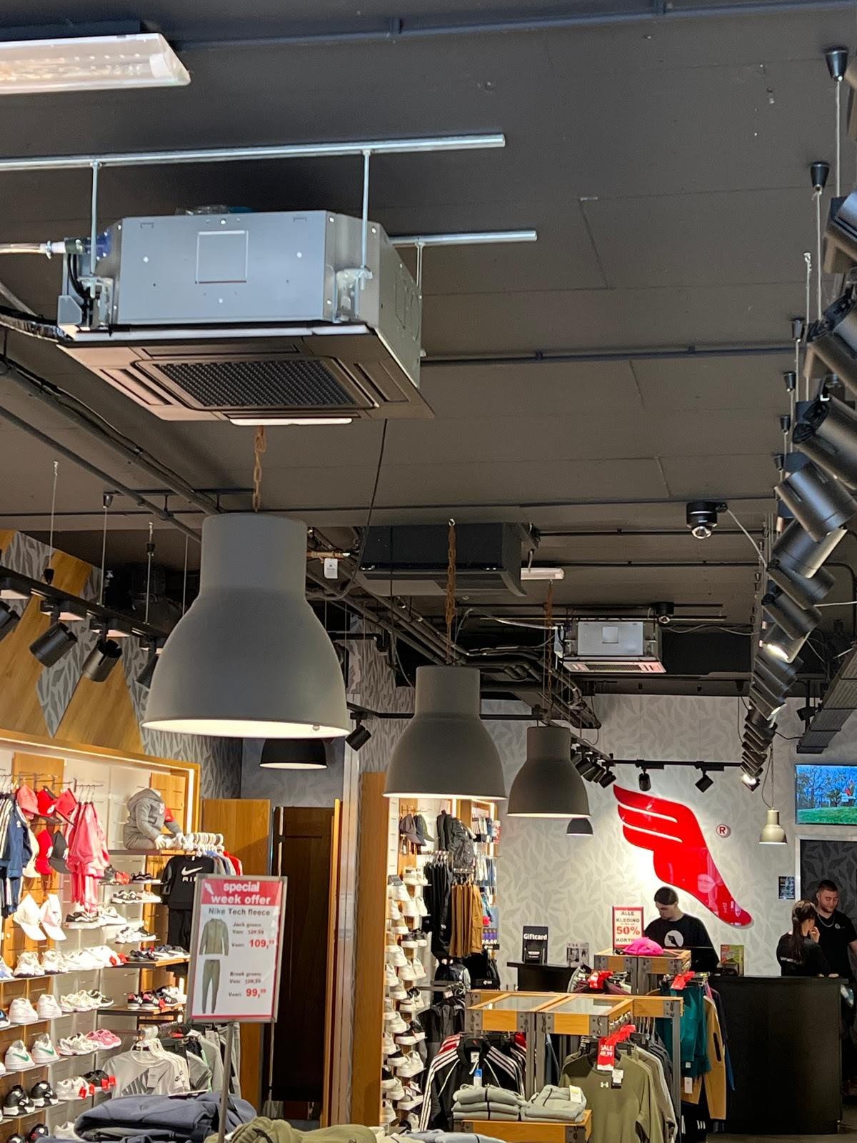 Interior of a retail store with industrial ceiling-mounted HVAC units, pendant lights, and merchandise displays below