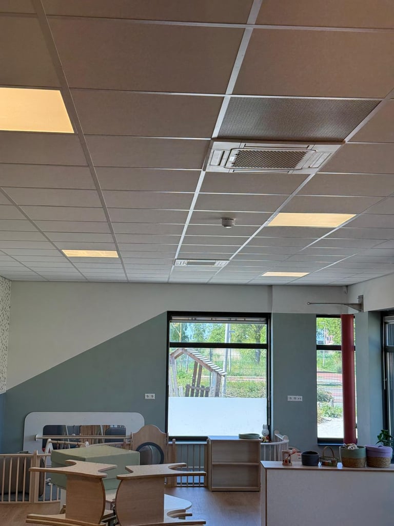Interior of an office space with drop ceiling tiles, recessed lights, desk area with computers, and large windows with natural daylight