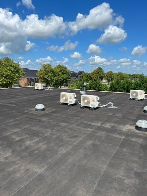 Rooftop with HVAC units under blue sky with white clouds, overlooking residential neighborhood