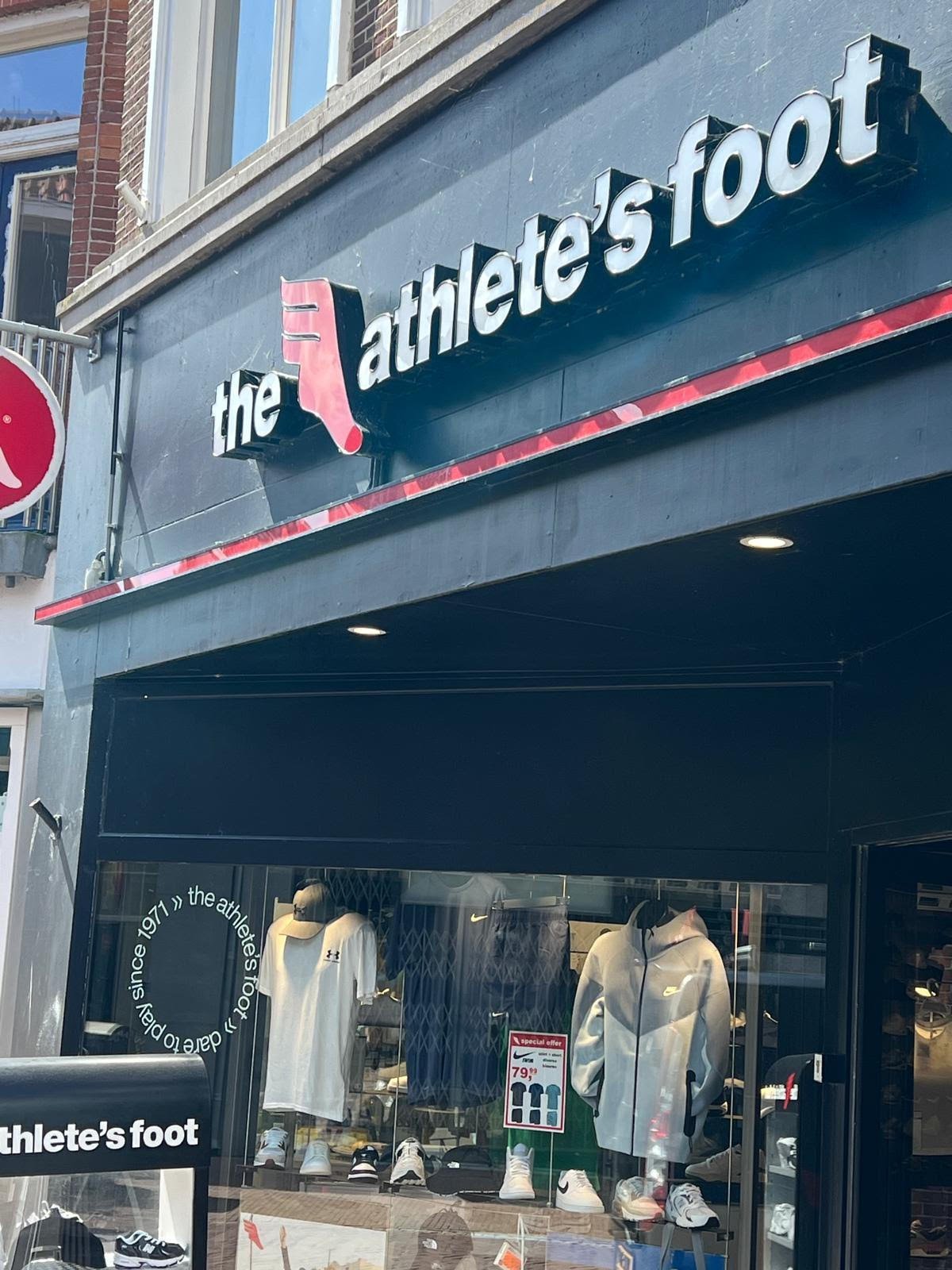 Storefront of the athletes foot shoe store with navy blue facade, white signage, and display window showing shoes and apparel