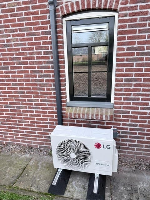LG heat pump outdoor unit mounted on concrete pad against red brick wall below window