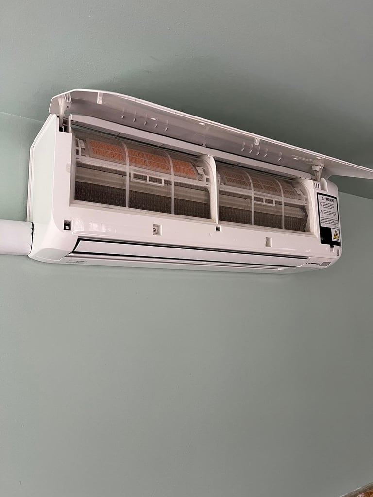 A white wall-mounted split air conditioning unit with visible front panels and control panel mounted on a light green wall.
