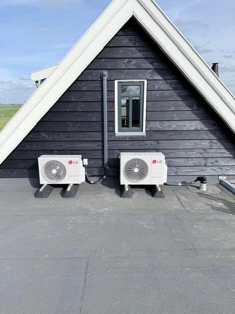 Modern black and white A-frame building with two LG air conditioning units mounted on the dark wooden exterior wall