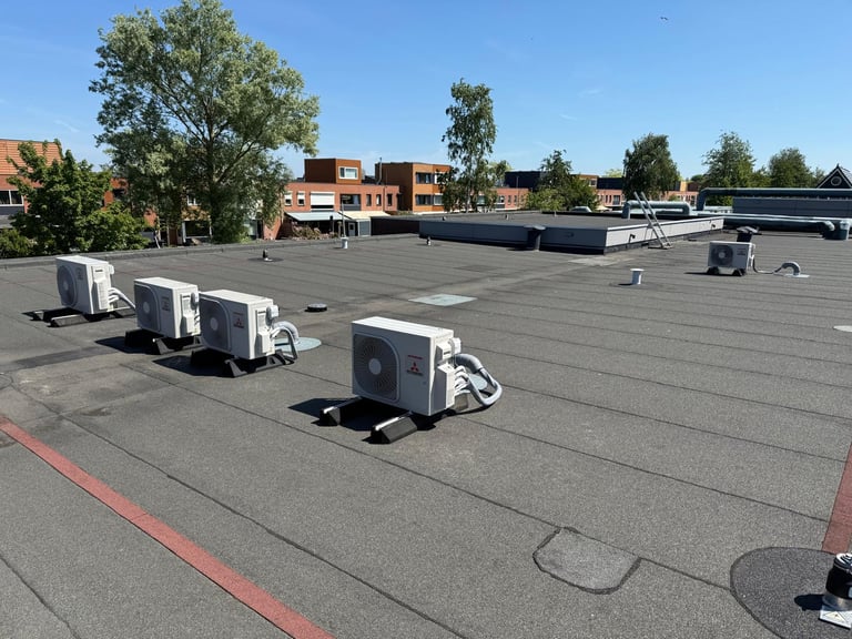 HVAC units and equipment installed on flat commercial building roof with clear sky and residential buildings visible in background