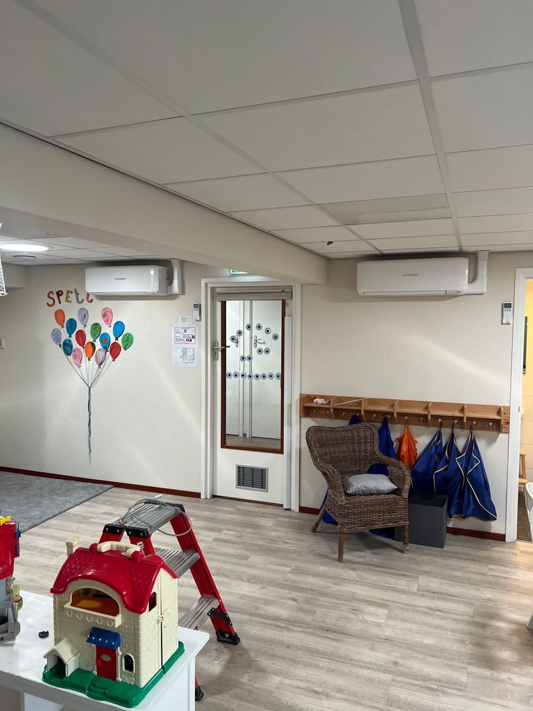 Interior of a classroom with colorful balloon wall art, toy house on table, and wooden cubbies with hanging items along the wall