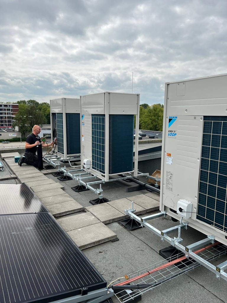 Technician working on rooftop HVAC units installed on a commercial building roof with cloudy sky