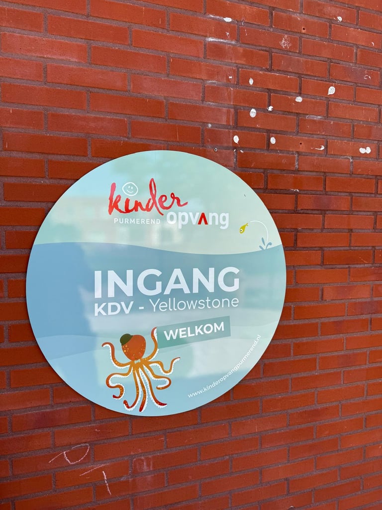 Circular welcome sign for Kinder Daycare KDV Yellowstone mounted on a red brick wall, featuring an orange octopus illustration