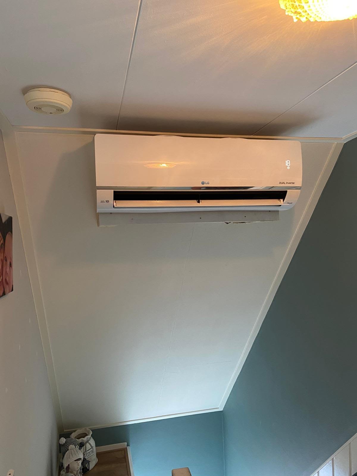 White LG split air conditioning unit mounted on a wall with ceiling smoke detector visible