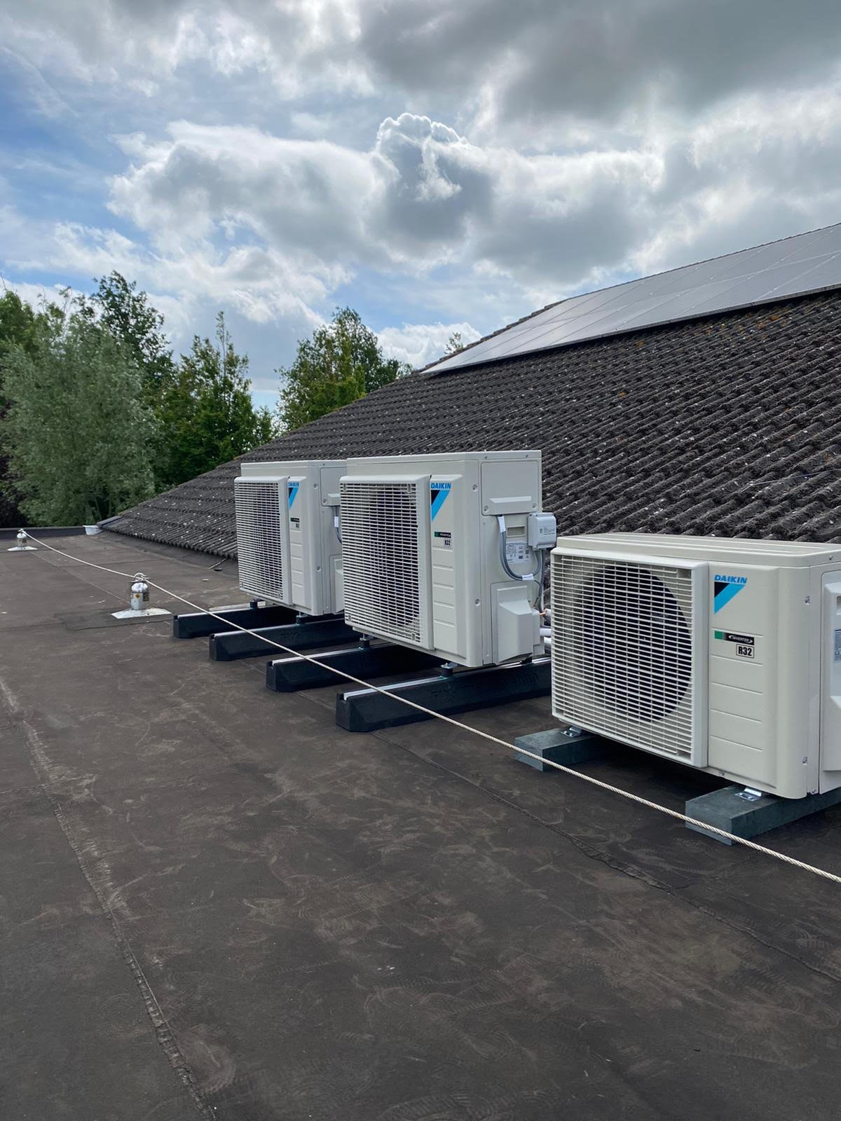 Rooftop HVAC units lined up on a building with dark shingles under cloudy sky