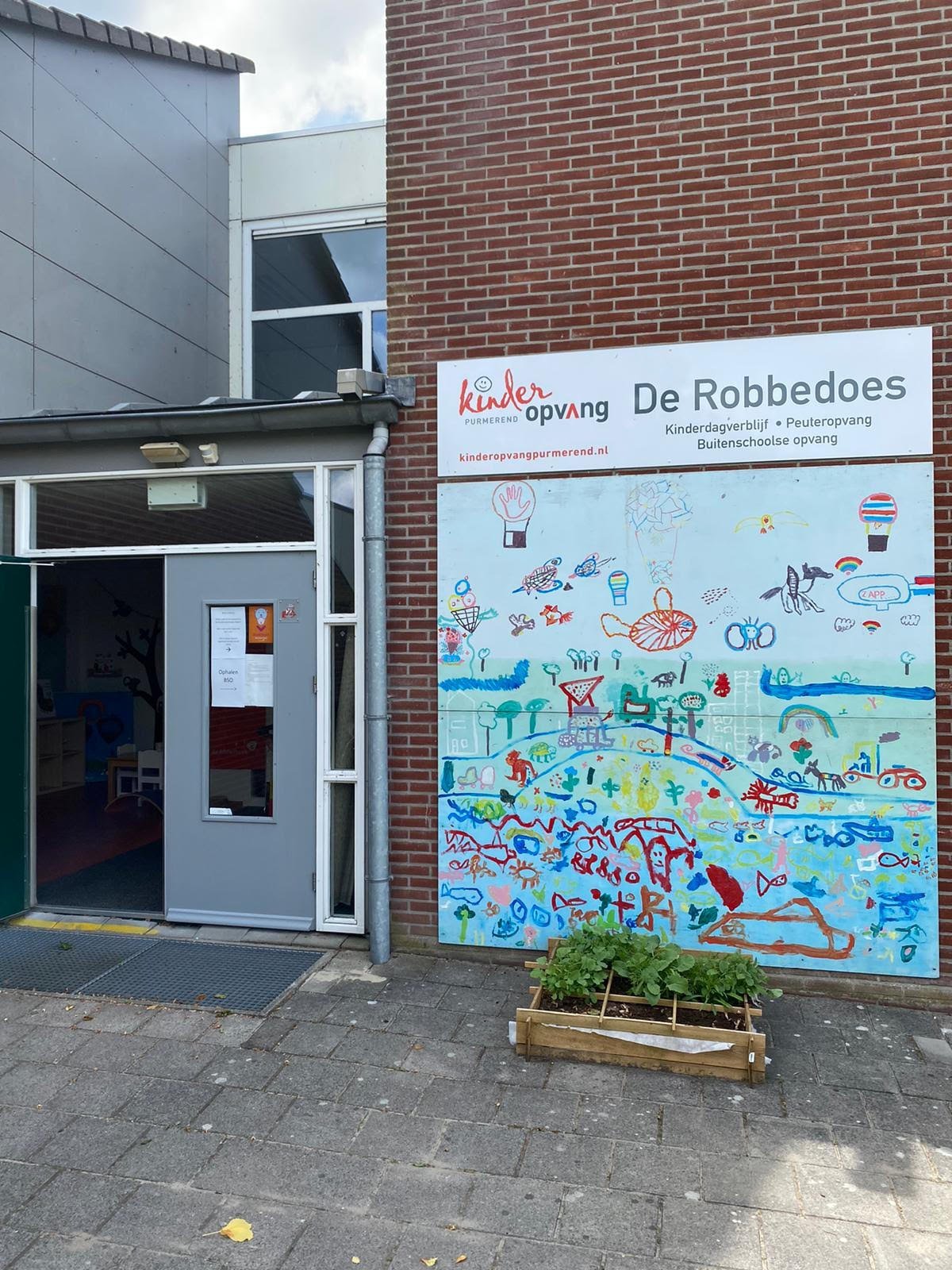 Exterior of De Robbedoes kindergarten with colorful childrens artwork mural on brick wall and glass entrance door