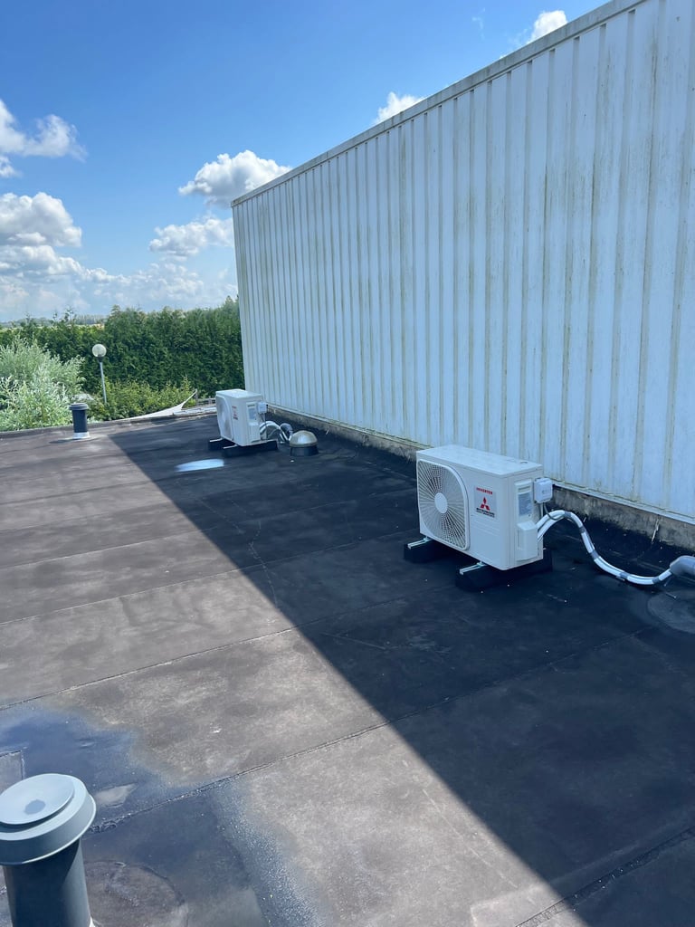 Flat commercial rooftop with HVAC units next to white metal building under blue sky