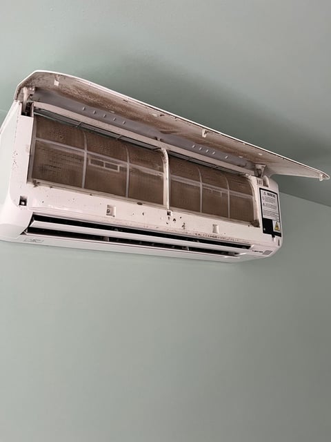 White wall-mounted air conditioning unit with open front panel exposing internal filters and components against gray wall