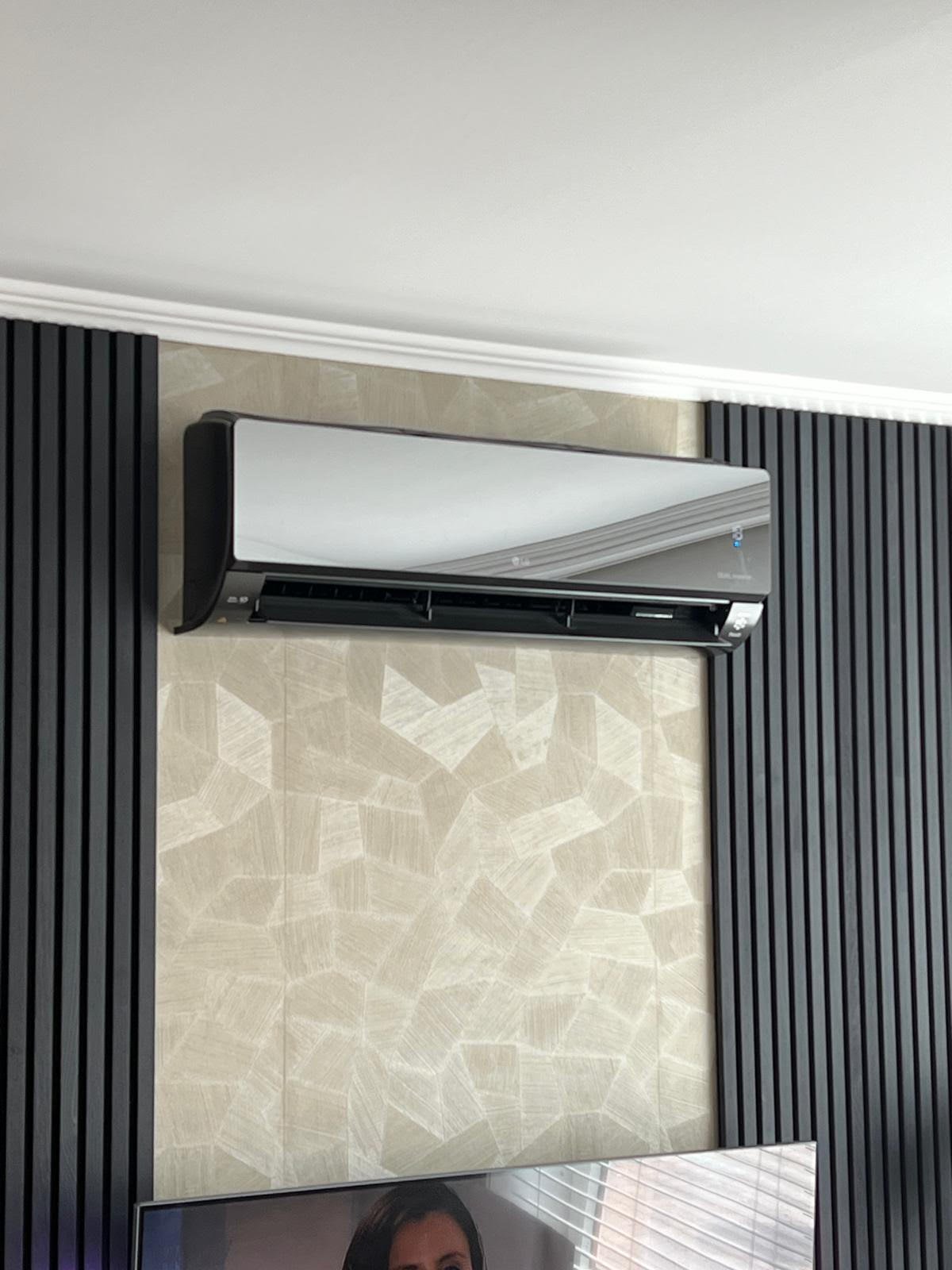 Indoor air conditioning unit mounted on beige textured wall with dark vertical corrugated siding on both sides