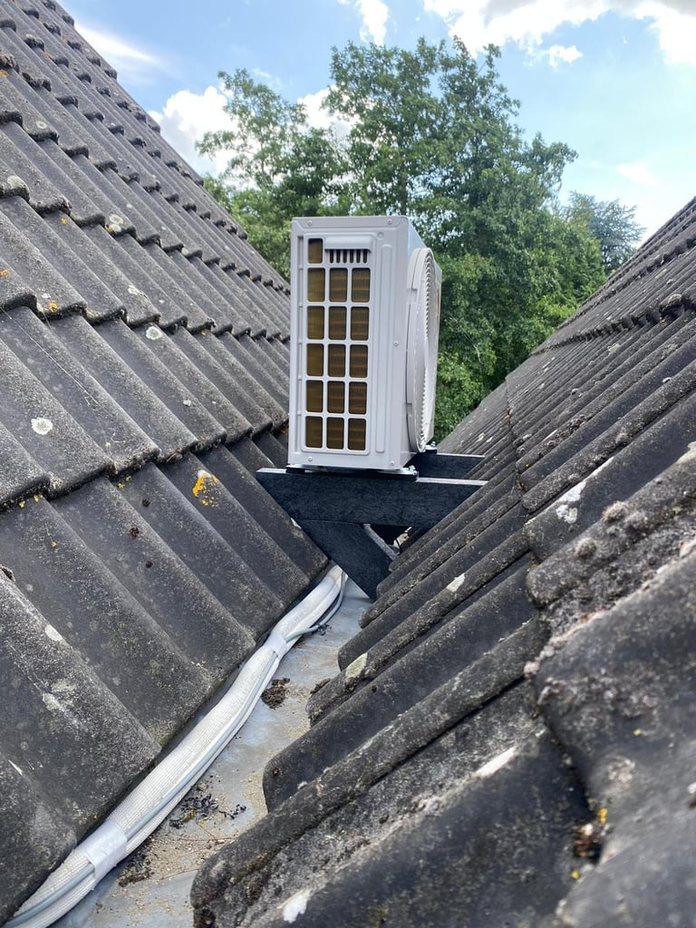 White dormer window installed on sloped roof with dark tiles and guttering, surrounded by green trees